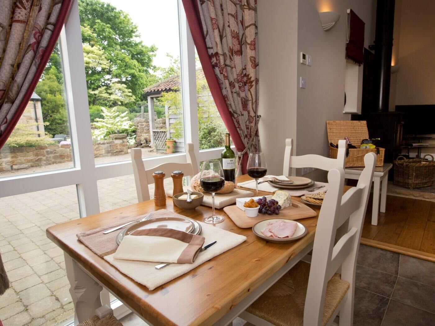 A dining table set with plates, glasses, and a bottle of wine, with a view of greenery outside.