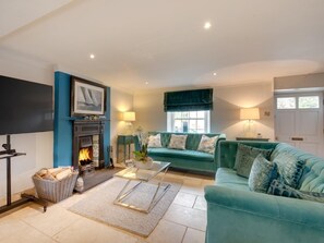 A living room with a fireplace, teal sofa, and a flat-screen TV. - 6 Bed in Richmond (oc-g0178) (Gilling West)