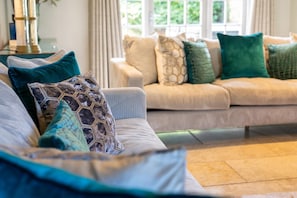 Ein Wohnzimmer mit einem beigen Sofa, gemusterten Kissen und einem Glastisch.