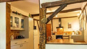 Een keuken met houten balken, een wit kastje met glazen deuren, een houten eiland en een hangende pannendroger.