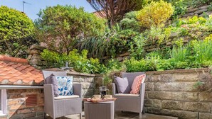 Eine Terrasse im Freien mit Korbmöbeln, einer Steinwand und verschiedenen Pflanzen.