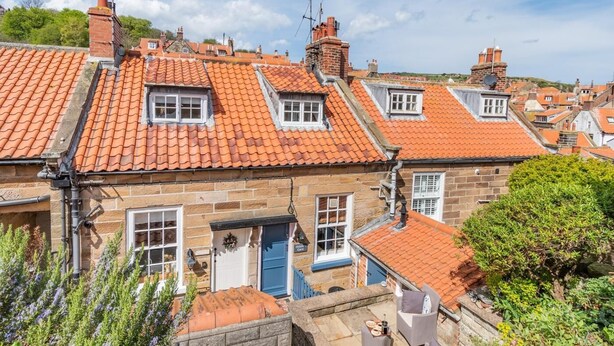 Ein traditionelles Steinhaus mit roten Ziegeldächern, zahlreichen Fenstern und einer kleinen Außenbereich-Sitzgelegenheit.