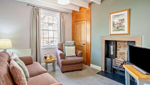 Ein gemütliches Wohnzimmer mit Kamin, Sofa, Sessel und Fernseher.