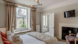Een slaapkamer met een groot bed, een open haard, een televisie en uitzicht op het omliggende landschap.