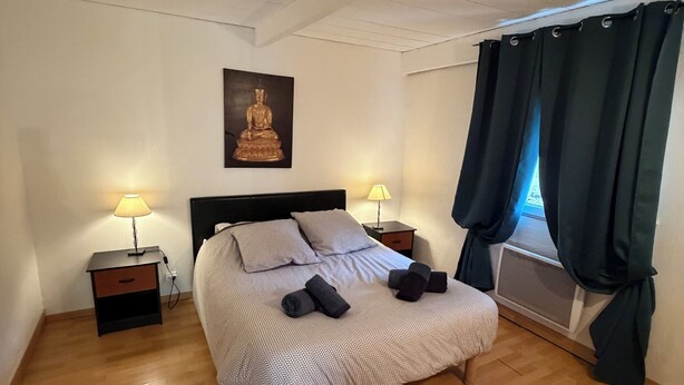 Ett sovrum med en säng, två sängbord, en vägglampa, ett fönster med gardiner och en Buddha-staty.