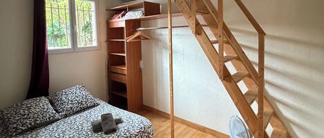 A room with a bed, a wooden staircase, a window, and a fan.