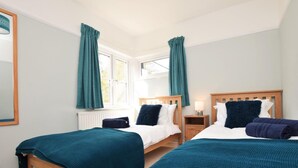Ein Hotelzimmer mit zwei Betten, blaustichigen Vorhängen, einem weißen Heizkörper und einem Fenster mit Blick.