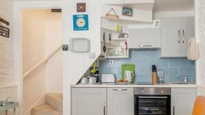 A compact kitchen with a microwave, toaster, and coffee maker on the counter, a small waiting area sign, and a staircase leading to another room. - 1 Bed in Brixham (oc-73940) (Brixham)