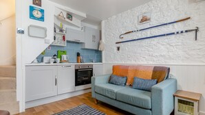 A compact living space with a kitchenette, a sofa, a small table, and a wall-mounted rack with items. - 1 Bed in Brixham (oc-73940) (Brixham)