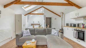 A modern loft-style room with a large gray sectional sofa, a wooden coffee table, a kitchenette, and a visible bedroom in the background. - 1 Bed in Taunton (oc-74145) (Williton)