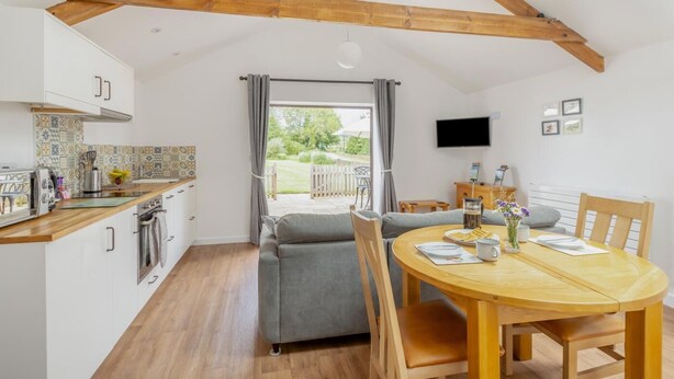 A compact kitchen with a dining area, wooden beams, a TV, and a view to the outside. - 1 Bed in Taunton (oc-74145) (Williton)