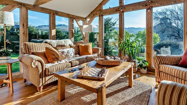 Amplia sala de estar con techo de madera, ventanas grandes, un conjunto de sofás, una mesa de centro y un tablero de ajedrez.