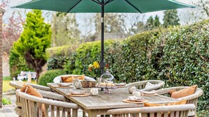 Un área de comedor al aire libre con una mesa de madera, sillas y un paraguas verde.