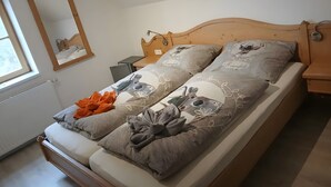 A neatly made bed with a headboard, a bedside table, a mirror, and a window.
