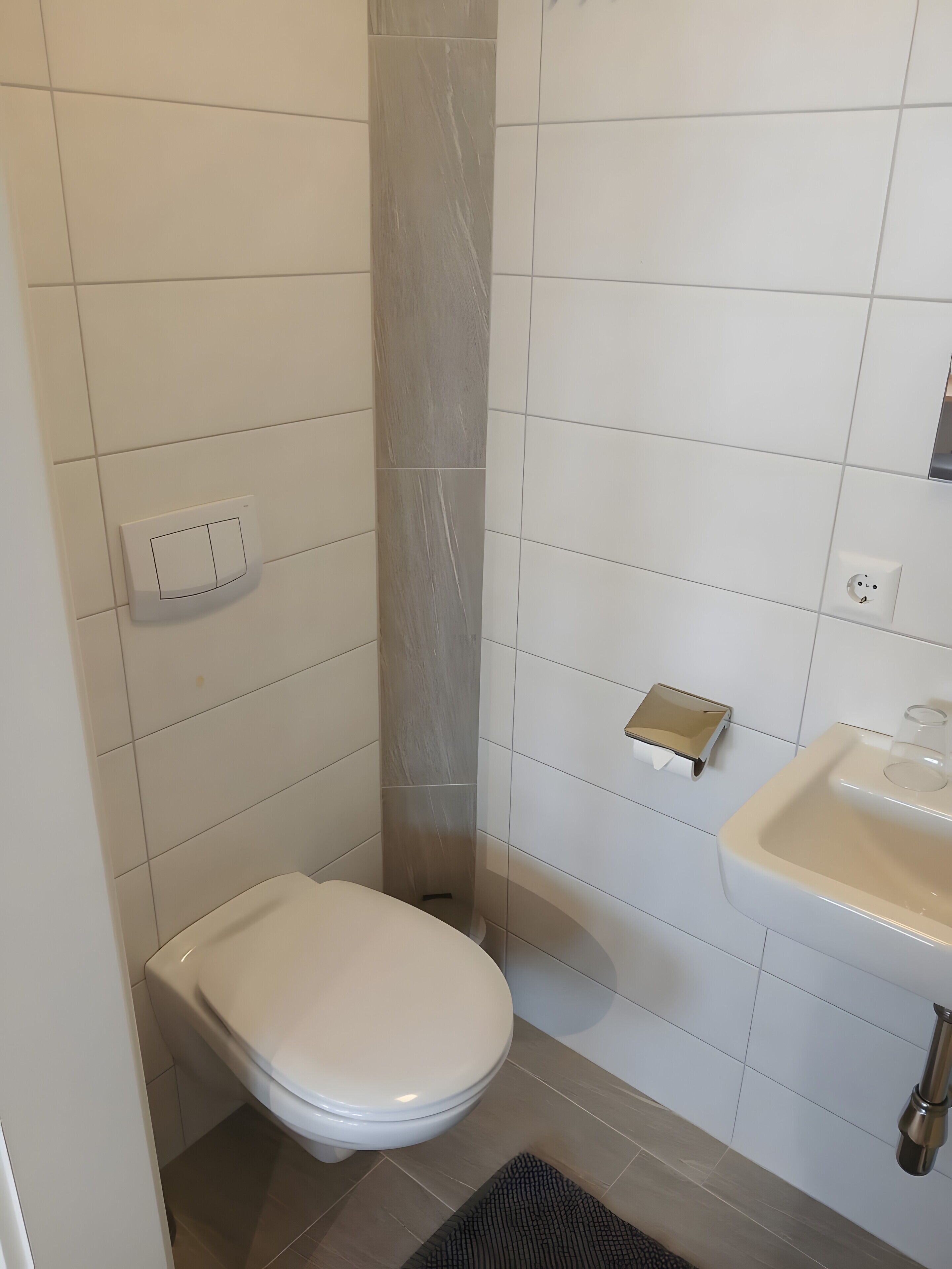 Een compacte badkamer met toilet, wastafel en zeepdispenser.