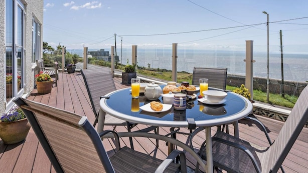 A round table with chairs on a wooden deck, overlooking a body of water. - 4 Bed in Bridgend (oc-74236) (Ogmore-by-Sea)
