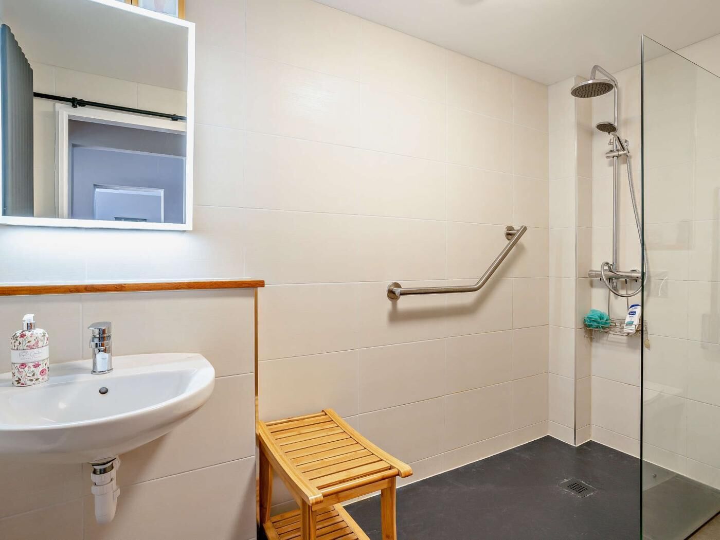 A bathroom with a sink, mirror, shower, and grab bar.