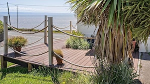 A coastal view with a wooden deck, rope barrier, and potted plants. - 4 Bed in Bridgend (oc-74236) (Ogmore-by-Sea)