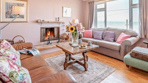 A living room with a fireplace, a sofa, a coffee table, and a view of the sea. - 4 Bed in Bridgend (oc-74236) (Ogmore-by-Sea)