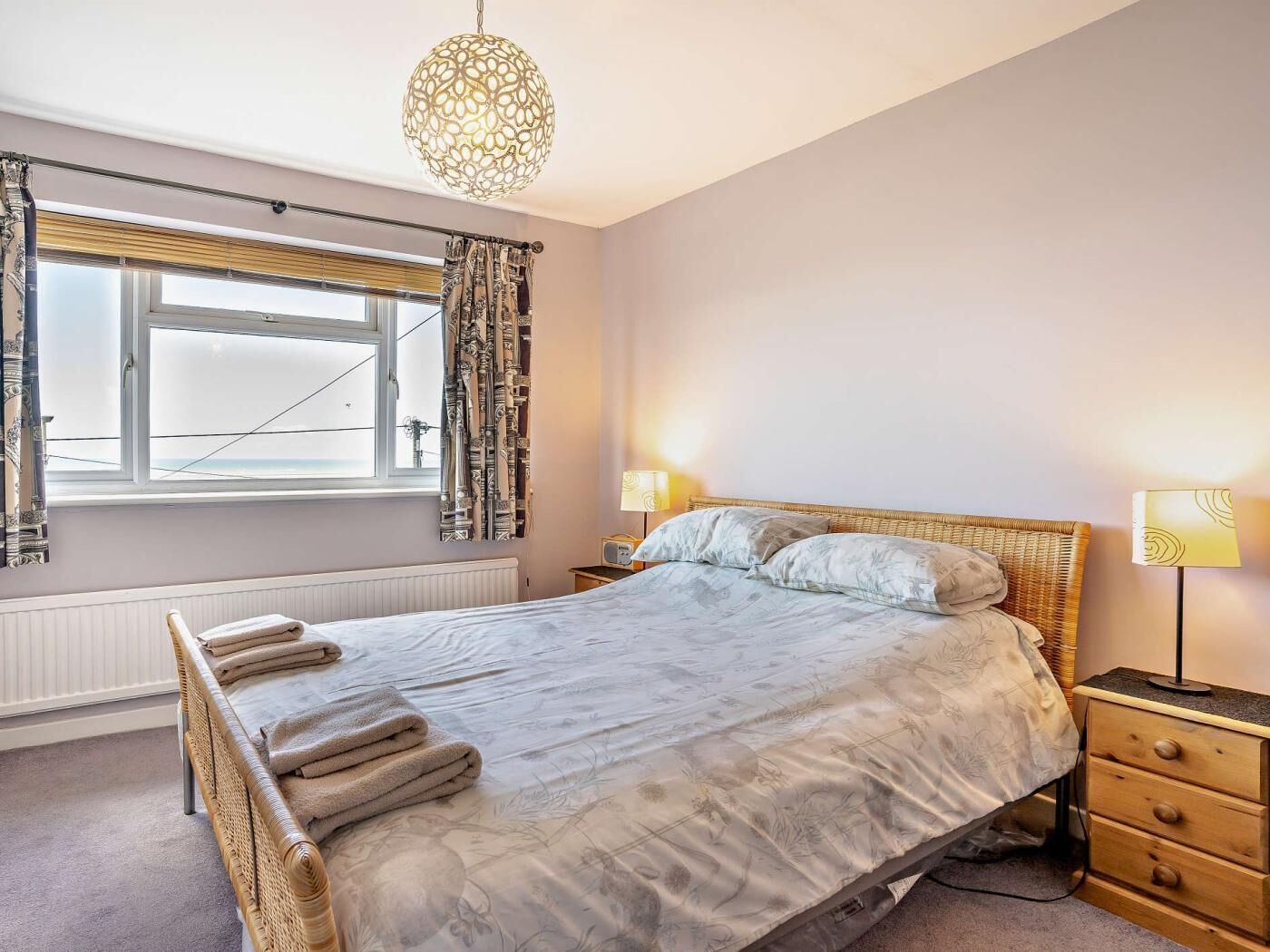 A bedroom with a bed, a window with curtains, a bedside lamp, and a hanging light fixture.