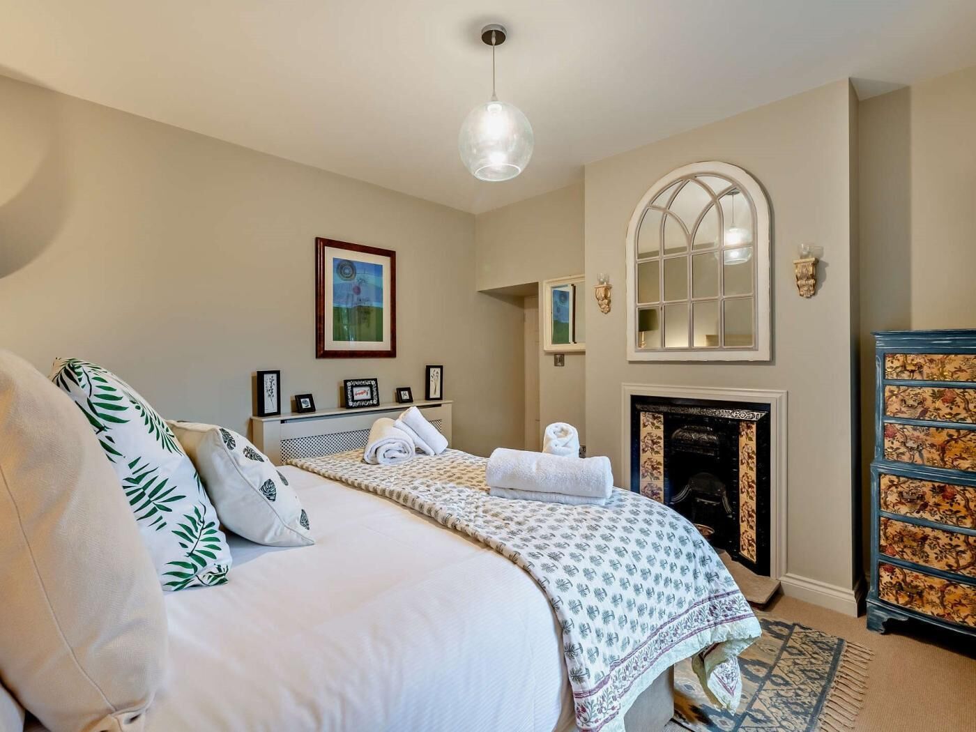 A bedroom with a bed, a fireplace, a mirror, and a dresser.