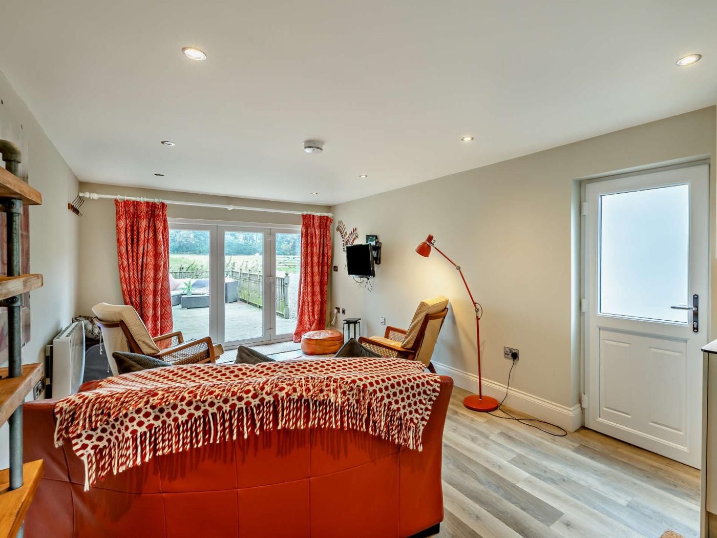 A bedroom with a bed, two chairs, a desk, a TV, and a door.