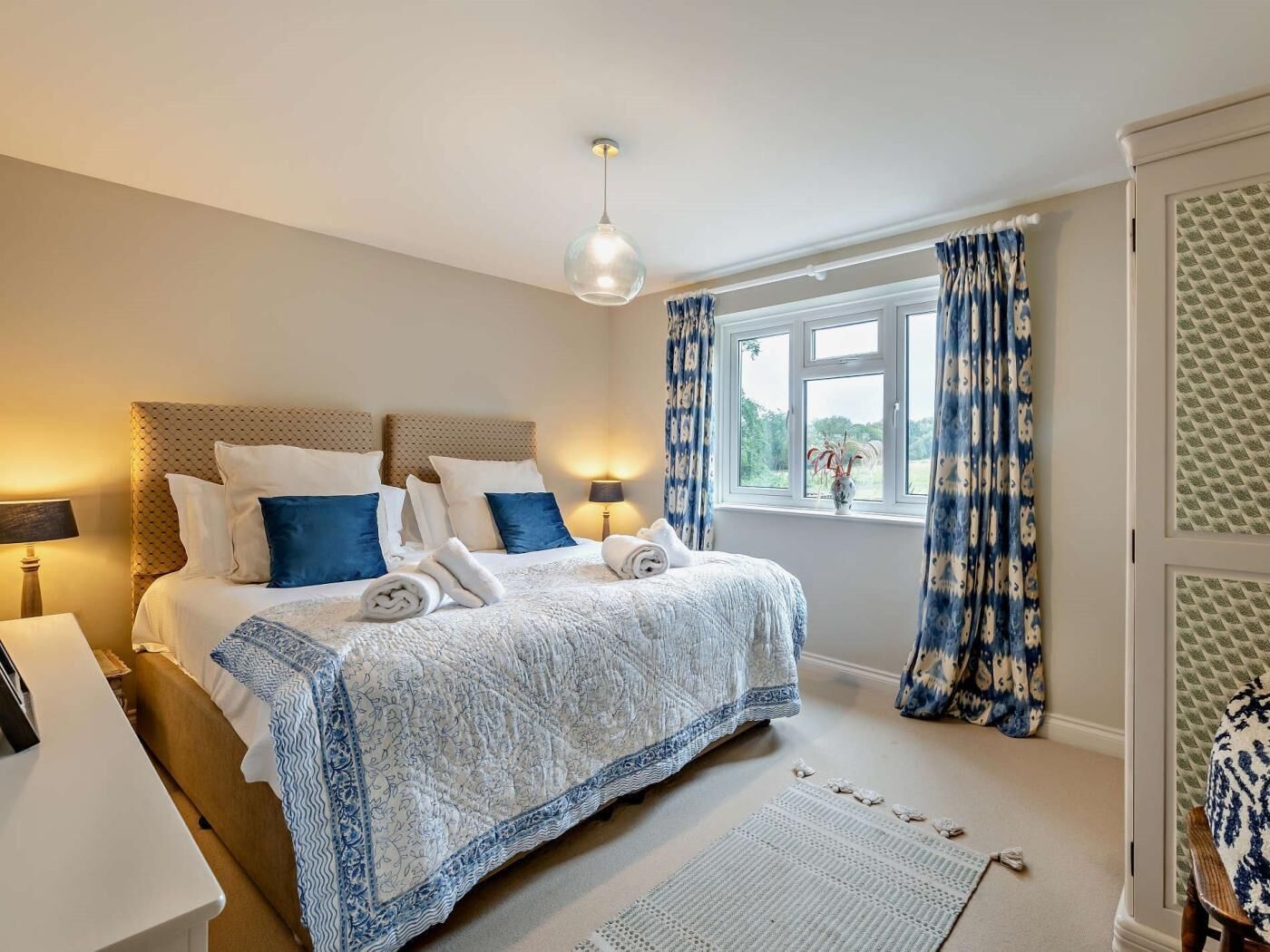 A bedroom with a bed, bedside tables, a window with curtains, and a view of greenery outside.