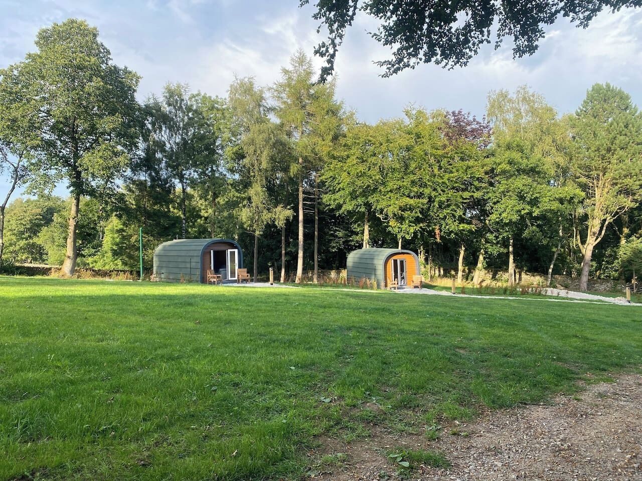 Two small, semi-open structures in a grassy area with trees in the background.