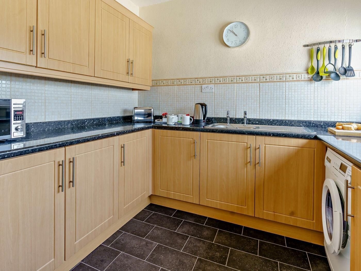 A kitchen with wooden cabinets, a microwave, a toaster, a sink, and a clock on the wall.
