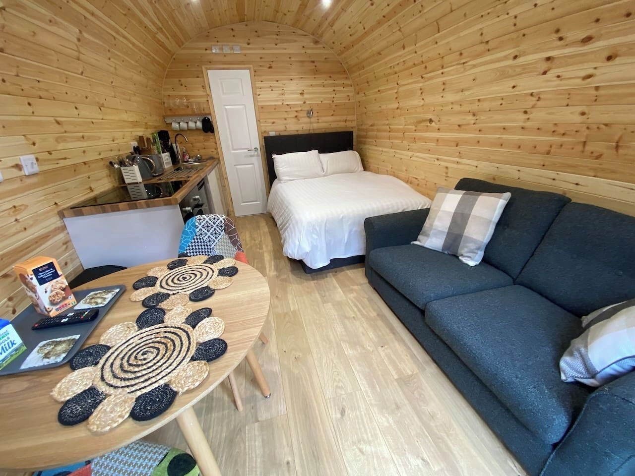 A cozy cabin interior with a bed, sofa, and a dining table with placemats.