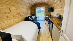 Interior de uma cabana de madeira com uma cama, um sofá, uma TV e uma kitchenette.