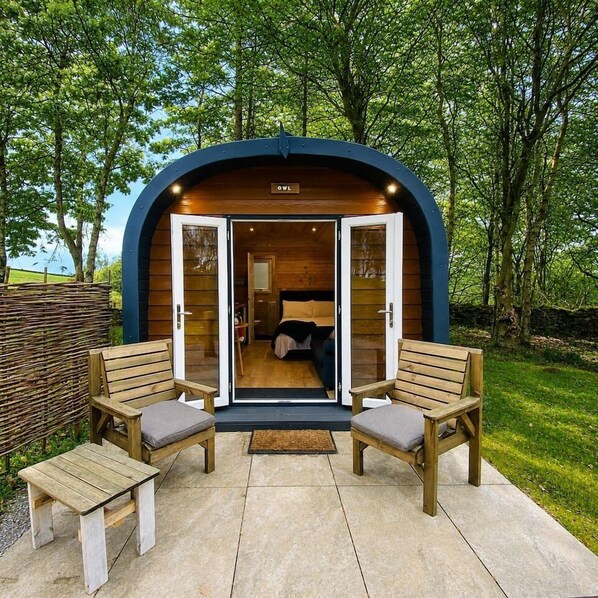 A cozy, semi-open wooden structure with a bed and two wooden benches outside.