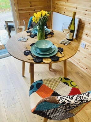 A round wooden table with a green centerpiece, a bottle of wine, and a vase of yellow flowers.