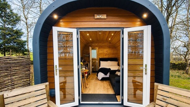 Uma cabana de madeira acolhedora e circular, com uma cama, uma mesa pequena e um banco.