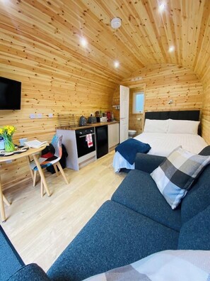 A cozy cabin interior with a bed, sofa, dining area, and kitchenette.
