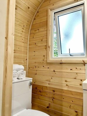 A wooden cabin bathroom with a window, a toilet, and a sink.