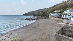 A coastal beach with a rocky shoreline, a row of seaside buildings, and a person walking along the beach. - 3 Bed in Torpoint (oc-74300) (Kingsand)