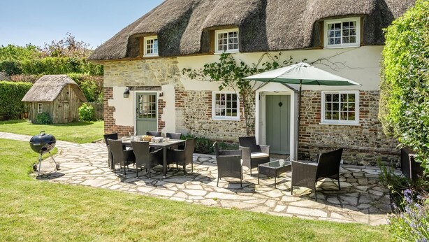 A thatched-roof house with a stone patio, outdoor seating, and a barbecue. - 3 Bed in Dorchester (oc-dc008) (Chaldon Herring)