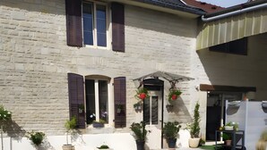 A two-story building with a stone facade, multiple windows with shutters, and potted plants.