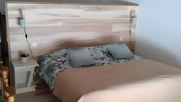 Slaapkamer met houten hoofdeinde, een bed met bloemenbeddengoed, een nachtkastje met lamp en een nachtkastje met stopcontact.