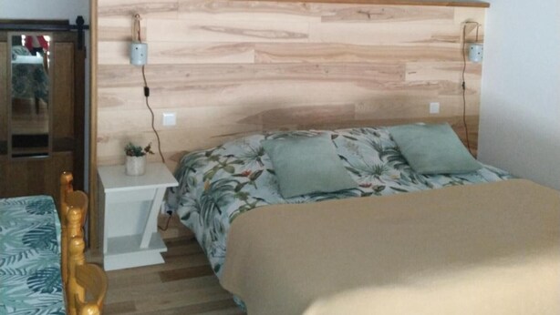 A bedroom with a wooden headboard, a bed with floral bedding, a nightstand, and a small table with a plant.