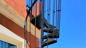 En balkong med ett vitt bord och stolar, en spiraltrappa och utsikt över avlägsna byggnader.