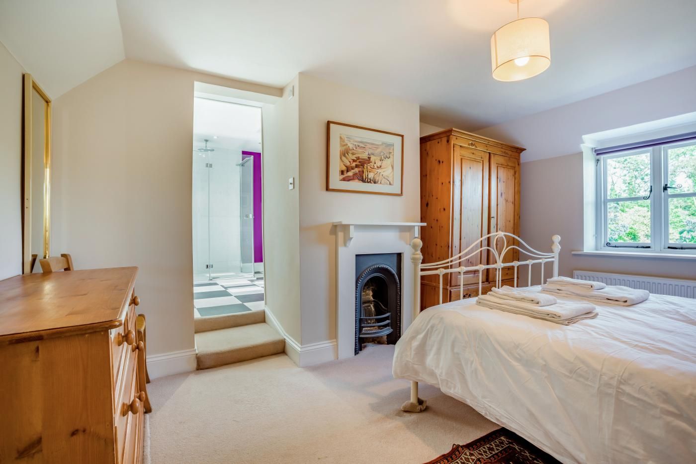 A bedroom with a bed, a fireplace, a wooden wardrobe, and a window with a view.