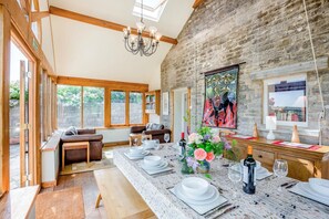 A dining area with a long table set for a meal, a chandelier, and a stone wall with artwork. - 5 Bed in Wareham (oc-dc061) (Woolgarston)