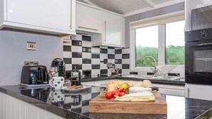 Eine moderne Küche mit Marmorarbeitsplatte, einem Holzer Schneidebrett mit Obst und Käse, einer Kaffeemaschine und Blick ins Grüne.