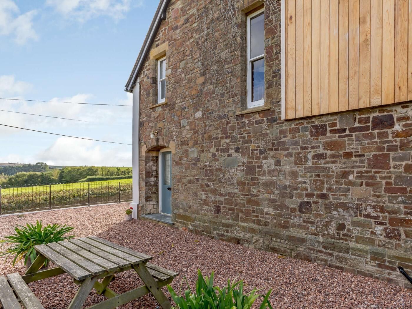 A stone building with a wooden door and windows, a gravel patio, and a wooden table.