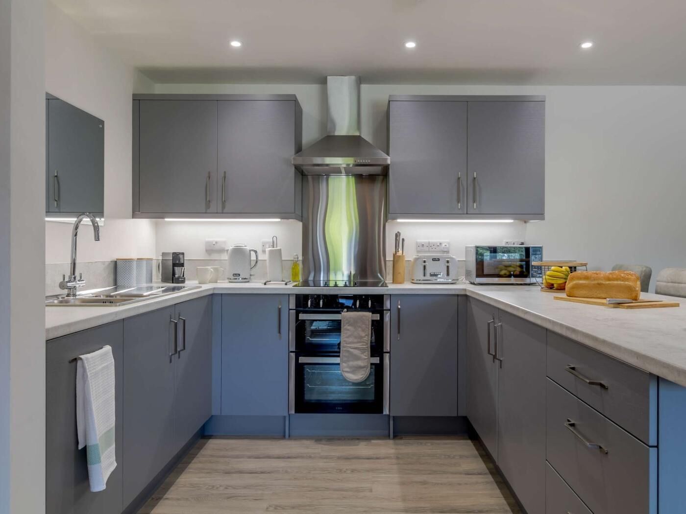 A modern kitchen with grey cabinets, a stainless steel range hood, a built-in oven, and a microwave.