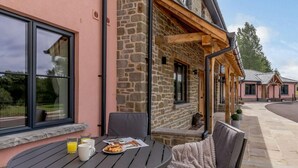 Ein Gebäude aus Stein mit einer rosafarbenen Fassade, Sitzgelegenheiten im Freien mit Tisch und Stühlen sowie eine überdachte Terrasse.