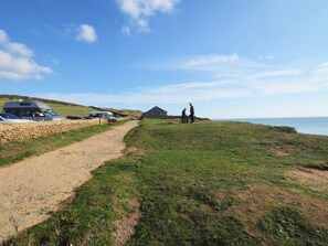 A coastal path leading to a grassy area with a stone wall and parked vehicles. - 1 Bed in Bridport (oc-dc178) (Burton Bradstock)