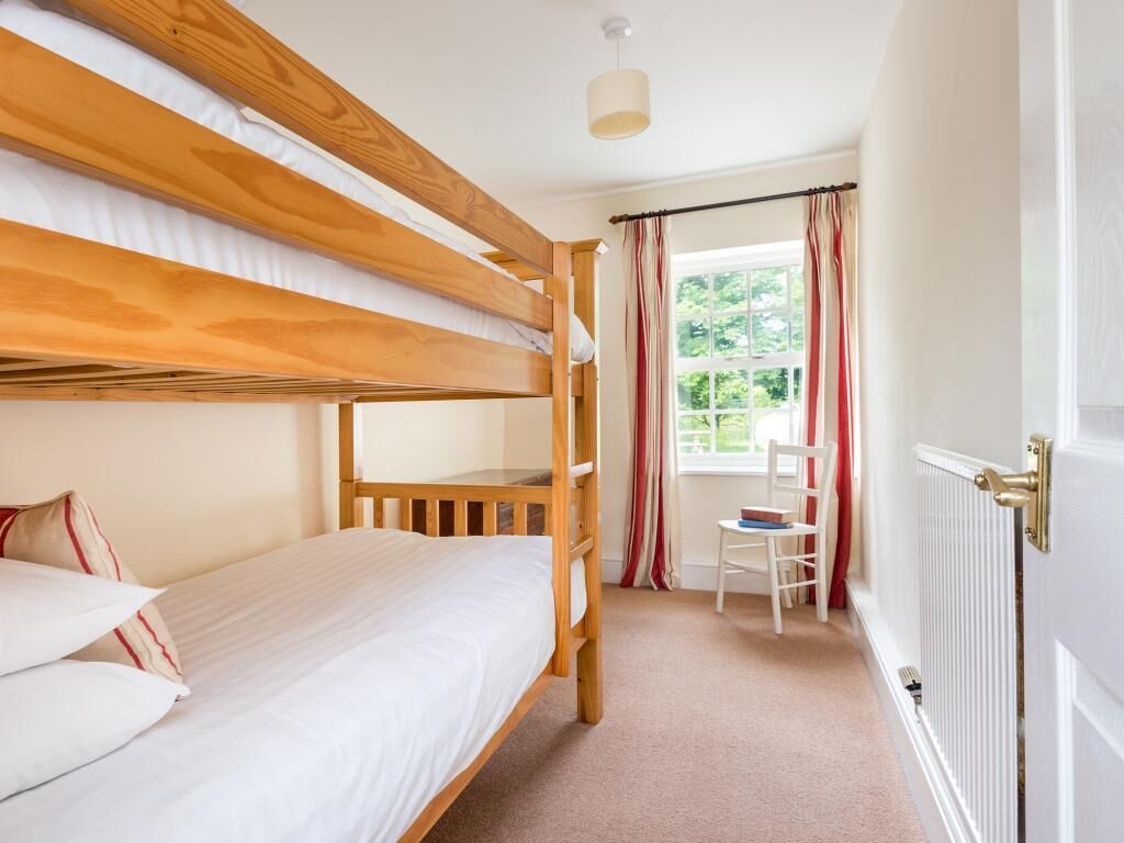 A bunk bed room with a window, a chair, and a radiator.